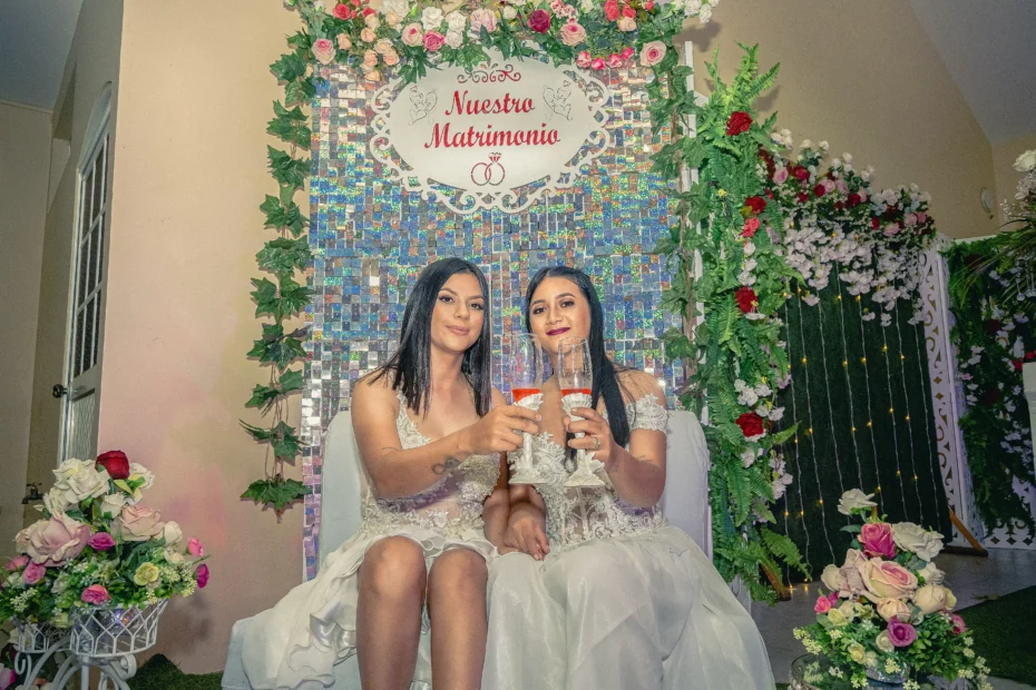 Dos mujeres sentadas con copas frente a una decoración de celebración