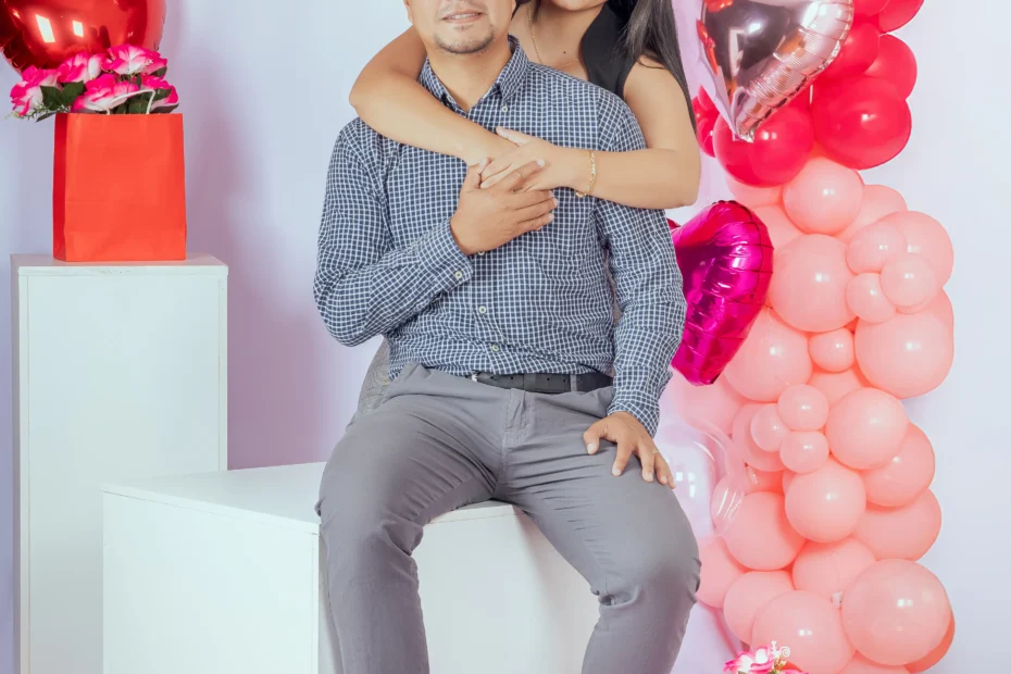 Pareja abrazada en un banco frente a una decoración con corazones