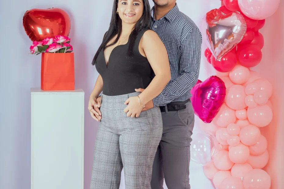 Pareja de pie frente a globos rojos y rosados con forma de corazón
