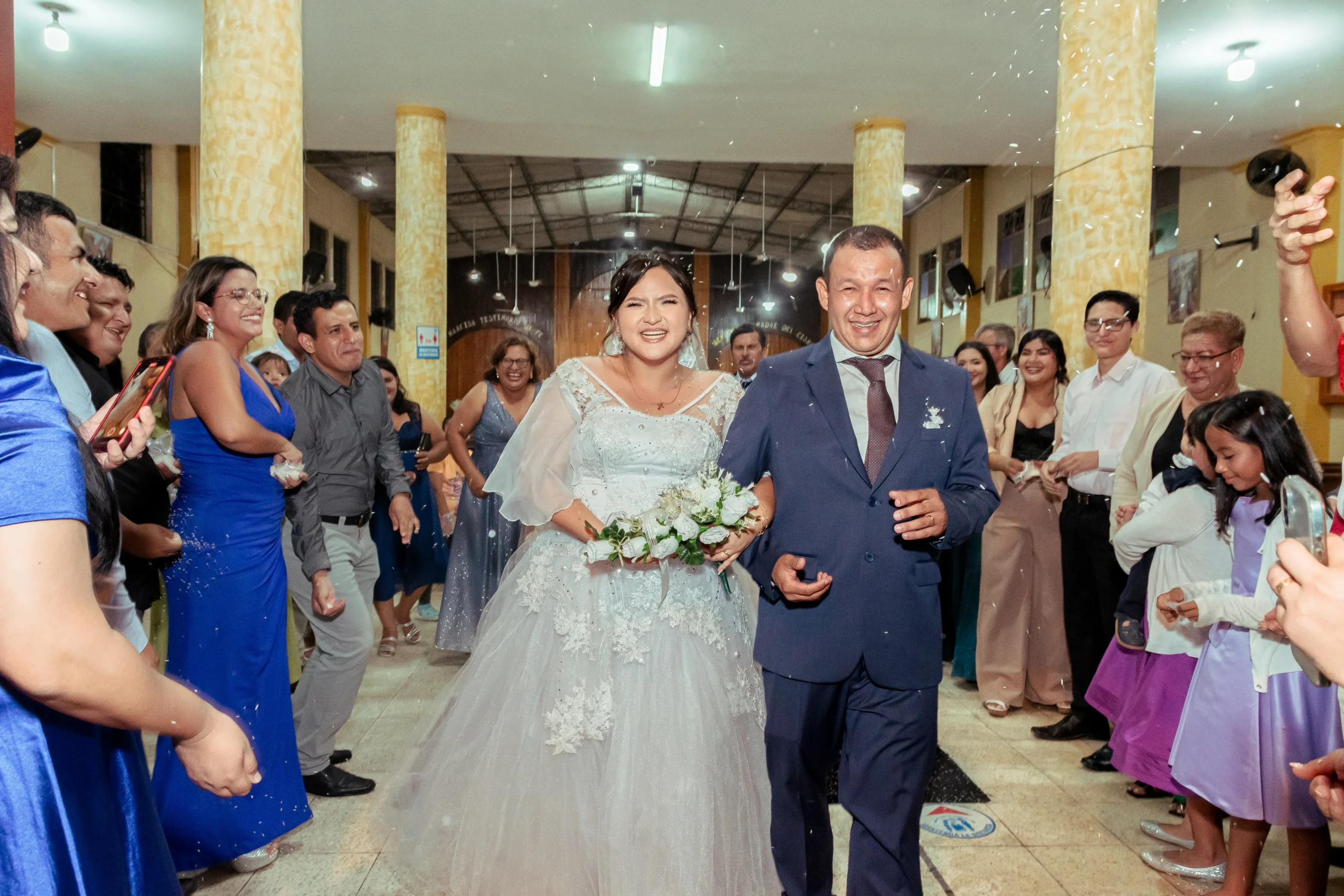 Pareja de recién casados saliendo junto a invitados que sostienen teléfonos