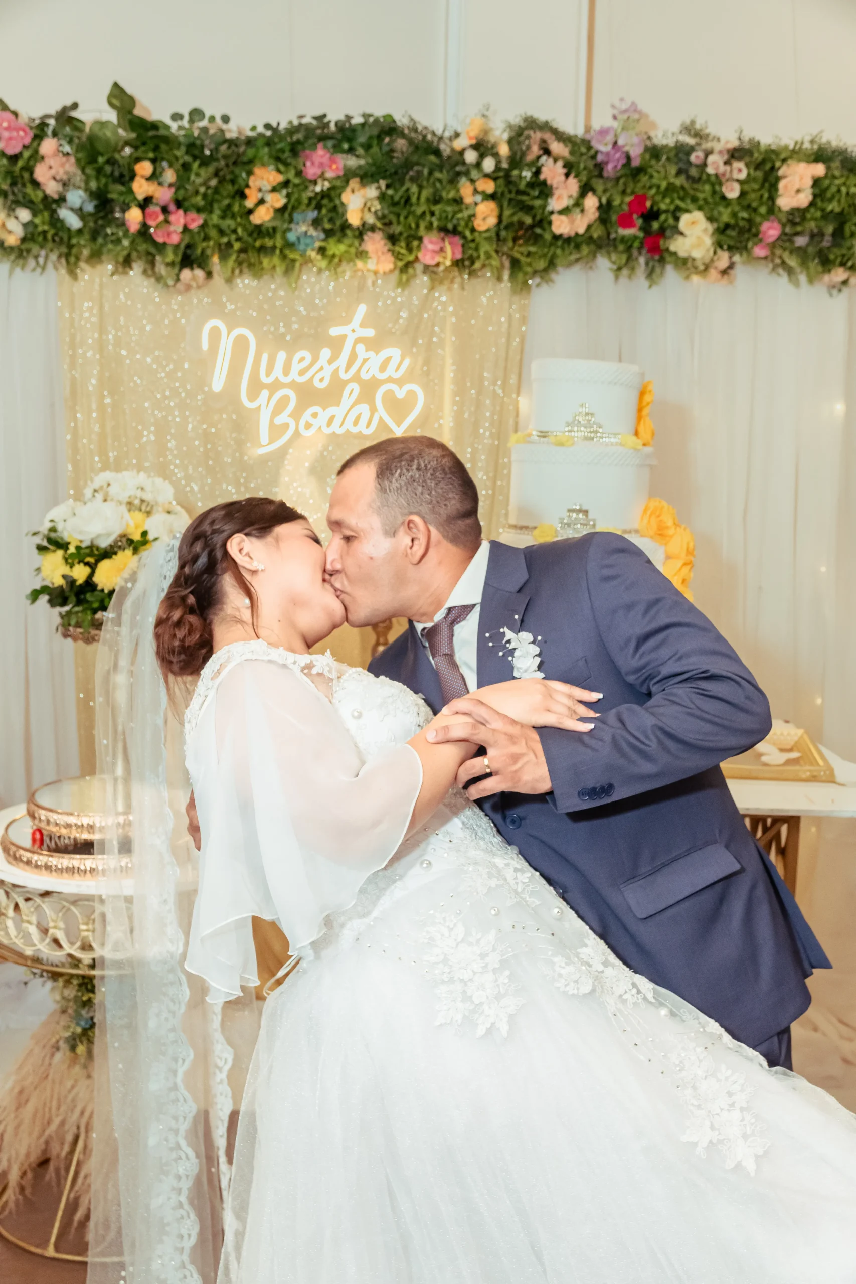 Pareja besándose frente a una decoración floral de boda